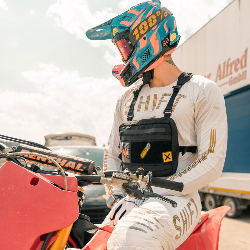 Person wearing a helmet and racing suit sitting on a red dirt bike with a blurred background.