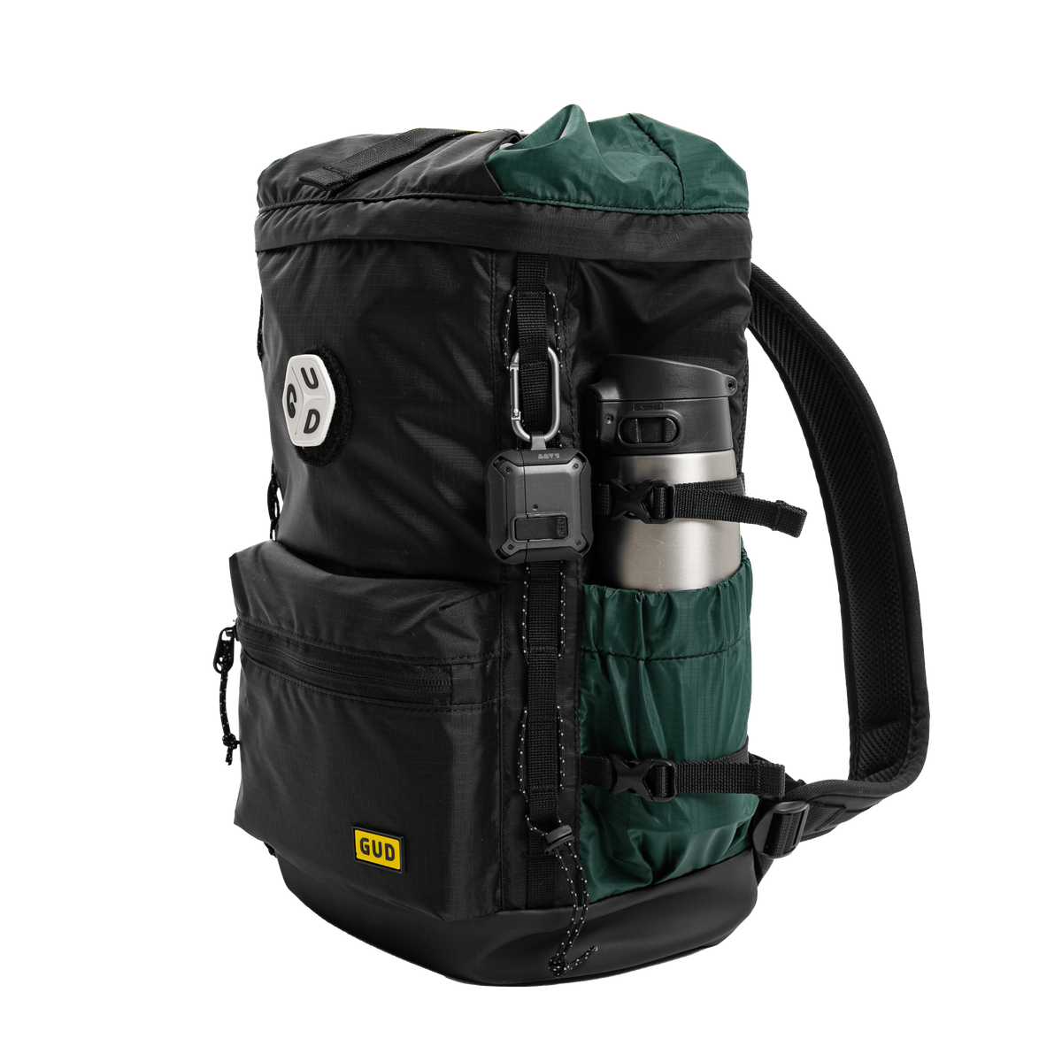 A black and dark green GUD backpack shown from a three-quarter angle on a white background, featuring a water bottle in its side pocket and a small action camera attached.